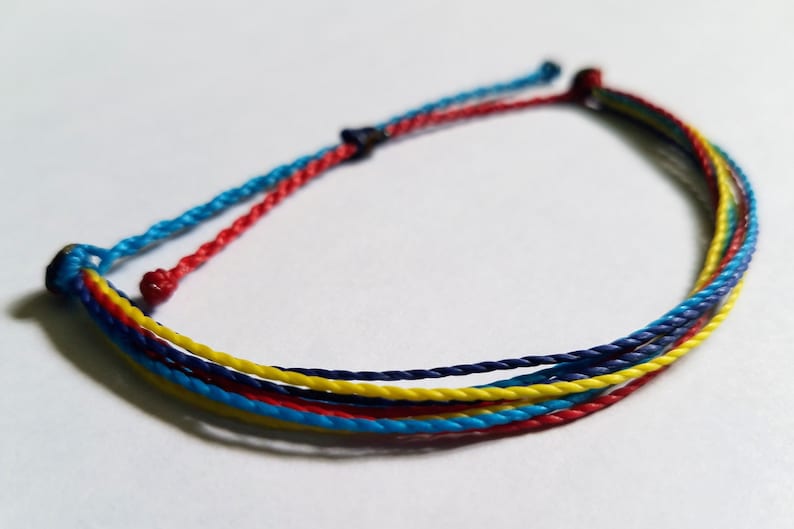 May include: A multi-colored friendship bracelet with blue, red, and yellow threads woven together.