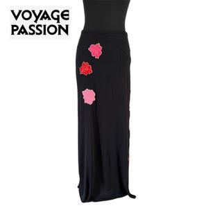 May include: Black maxi skirt featuring three floral appliqués in pink and red. The skirt has a high waist and a slight flare at the hem. The text "VOYAGE PASSION" is in the upper left corner.