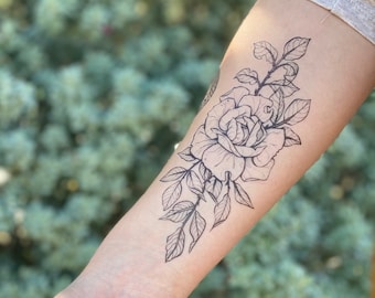 May include: A black and white temporary tattoo of a rose with leaves on a person's arm.