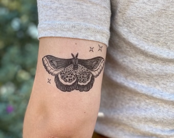 May include: A temporary tattoo of a black and white moth with a detailed design. The moth is surrounded by four small stars.