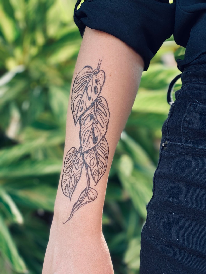 May include: A black and white temporary tattoo of a monstera plant with leaves in various sizes.