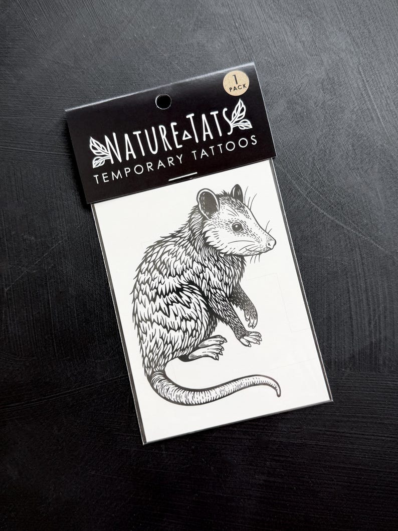 May include: A black and white temporary tattoo sheet featuring a detailed line art illustration of an opossum. The packaging header reads NATURE TATS TEMPORARY TATTOOS and includes a 1 PACK label. The design is printed on a white rectangular backing.