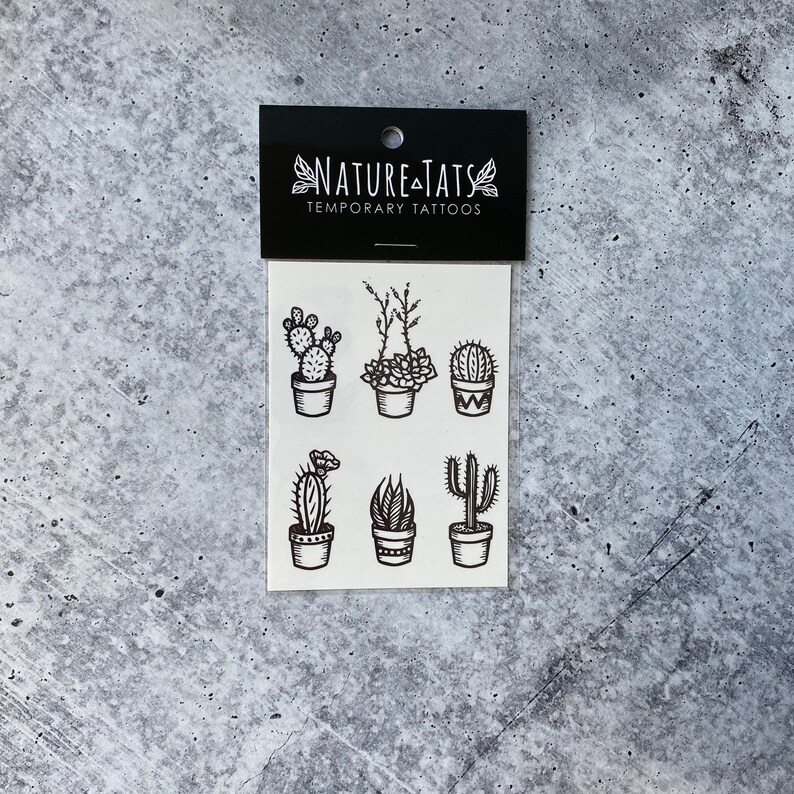 May include: A sheet of temporary tattoos featuring six different black and white illustrations of potted cacti and succulents. The sheet is labeled "Nature Tats Temporary Tattoos".