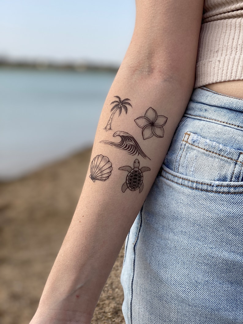 May include: Five black and white temporary tattoos on a person's arm. The tattoos are of a palm tree, a flower, a wave, a seashell, and a turtle.