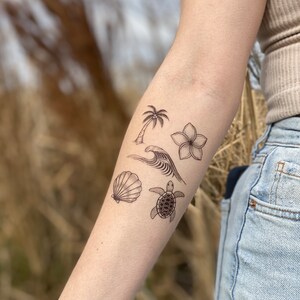 May include: A set of five temporary tattoos featuring a palm tree, a wave, a seashell, a flower, and a turtle. The tattoos are black and white and are designed to look like traditional line drawings.