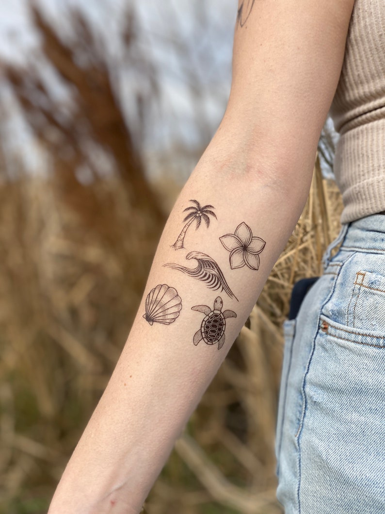 May include: A set of five temporary tattoos featuring a palm tree, a wave, a seashell, a flower, and a turtle. The tattoos are black and white and are designed to look like traditional line drawings.