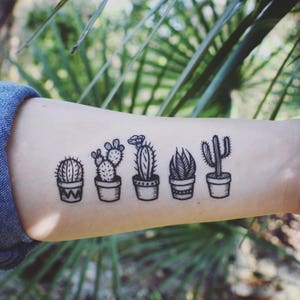 May include: A black and white line drawing of five potted cacti on a person's arm. The cacti are drawn in a simple style and are all different shapes and sizes.