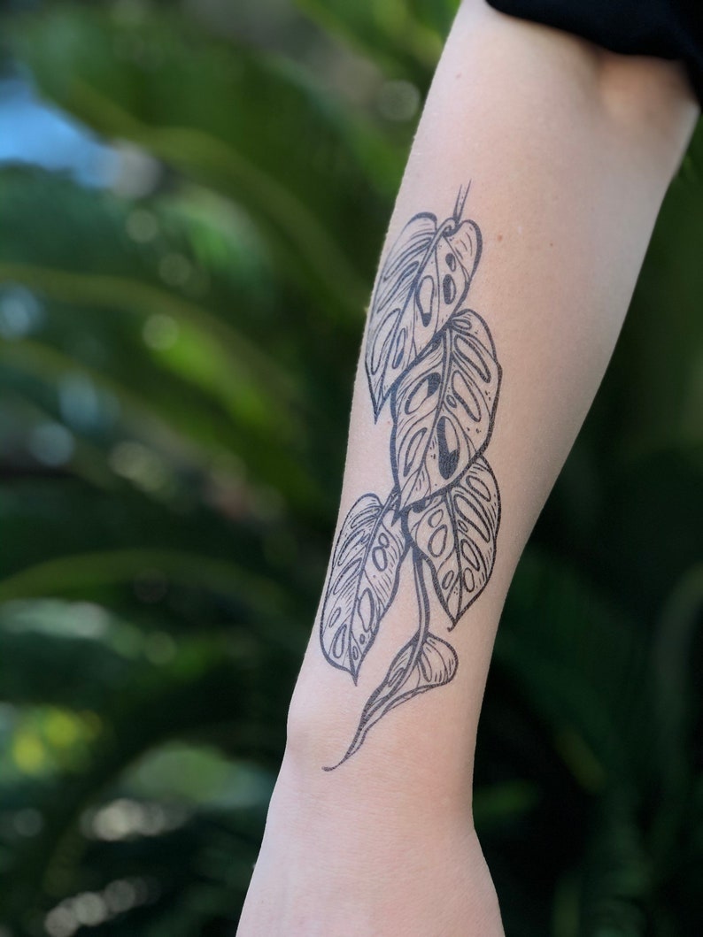 May include: Black and white temporary tattoo of a monstera plant with leaves in various sizes.