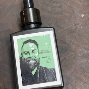 May include: A black glass bottle with a dropper top, labeled "Stephen's SUPER DELUXE Beard Oil with argan oil, jojoba oil, cedar oil". The bottle has a green background with a black and white illustration of a man with a beard.