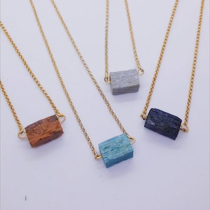 May include: Four gold chain necklaces with different colored wooden pendant charms. The charms are rectangular and have a natural wood grain texture. The colors are brown, gray, blue, and black.