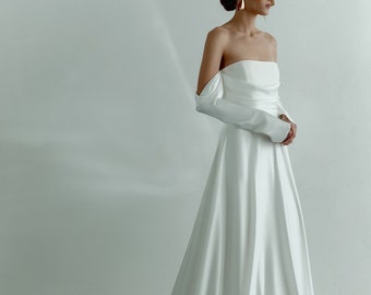 May include: A white off-the-shoulder wedding dress with long sleeves and a flowing skirt.