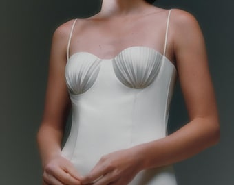 May include: A white, sleeveless, fitted dress with a sweetheart neckline and a scalloped bodice.