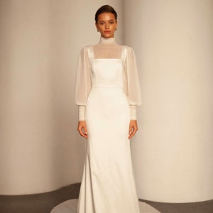 May include: A white wedding dress with a high neck and long sleeves. The dress has a fitted bodice and a flowing skirt.