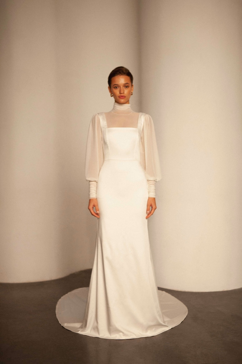 May include: A white wedding dress with a high neck and long sleeves. The dress has a fitted bodice and a flowing skirt.