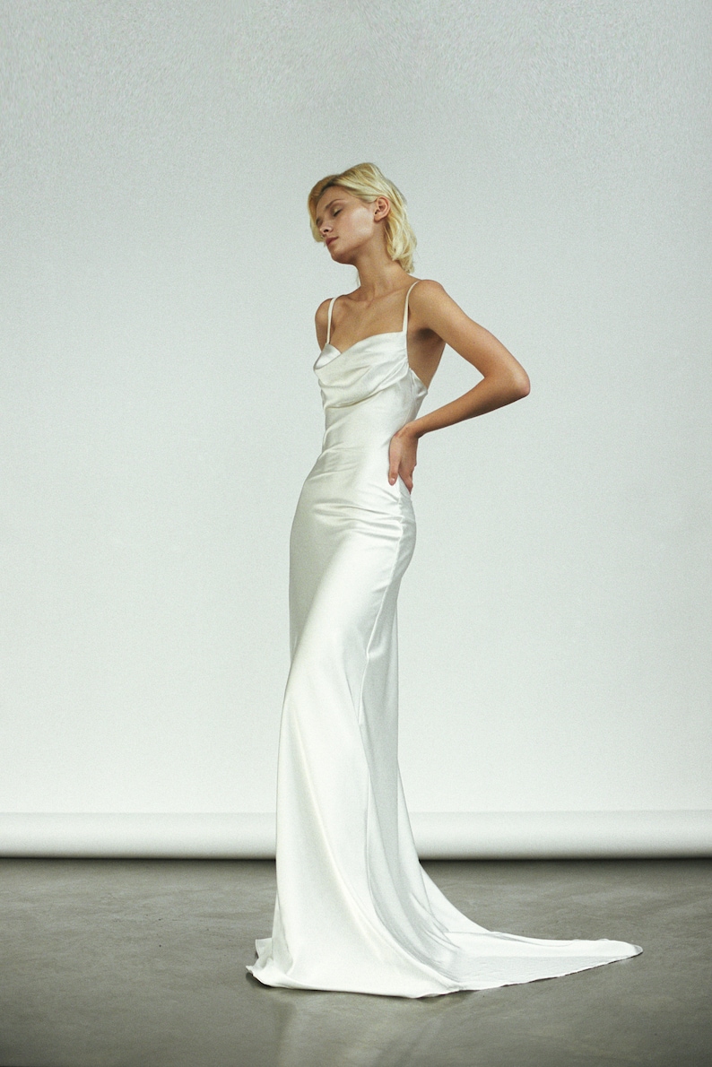 Peut inclure: Une robe blanche en satin avec un col en cowl et des bretelles spaghetti. La robe a un corsage ajust&eacute; et une jupe fluide.