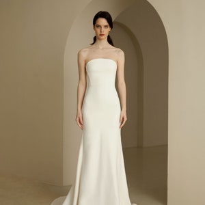 Puede incluir: Un sencillo vestido de novia blanco sin tirantes, con un corpi&ntilde;o ajustado y una falda fluida.