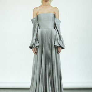May include: A gray off-the-shoulder gown with long, pleated sleeves and a flowing skirt.