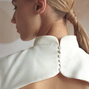 Puede incluir: Una blusa blanca con cuello alto y una fila de botones blancos en la espalda.