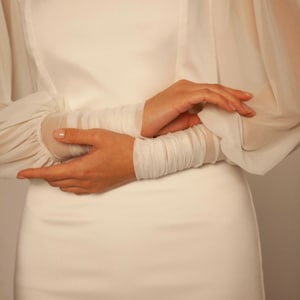 May include: A white dress with long sleeves and a fitted bodice. The sleeves are made of sheer fabric and have a gathered detail at the wrist.