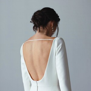 May include: A white, long-sleeved dress with a low back and a button closure down the back.