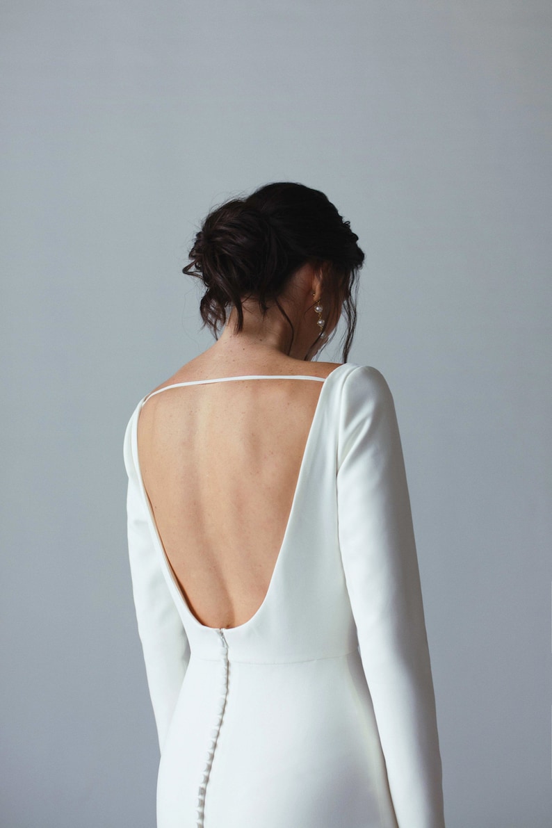 May include: A white, long-sleeved dress with a low back and a button closure down the back.