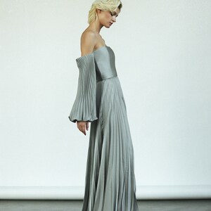 May include: A silver off-the-shoulder gown with pleated fabric and long sleeves.