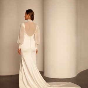 May include: A white wedding dress with a high neck and long sleeves. The dress has a fitted bodice and a flowing skirt.