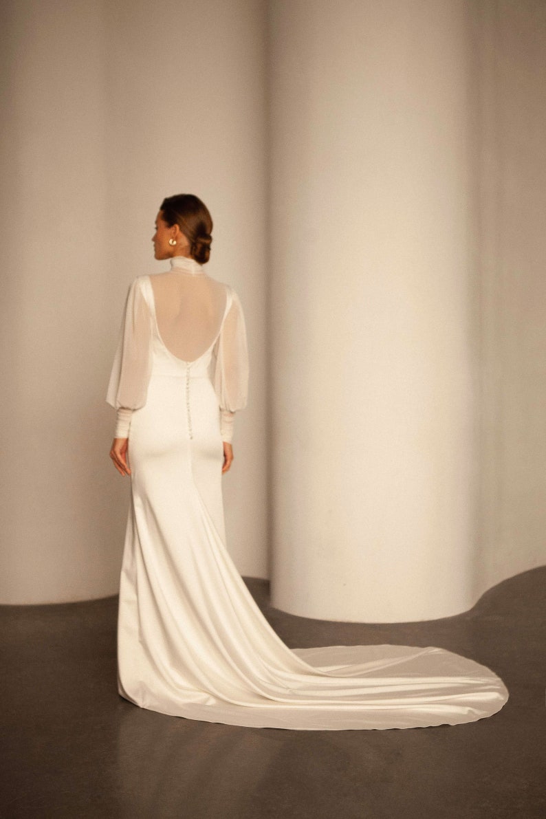 May include: A white wedding dress with a high neck and long sleeves. The dress has a fitted bodice and a flowing skirt.
