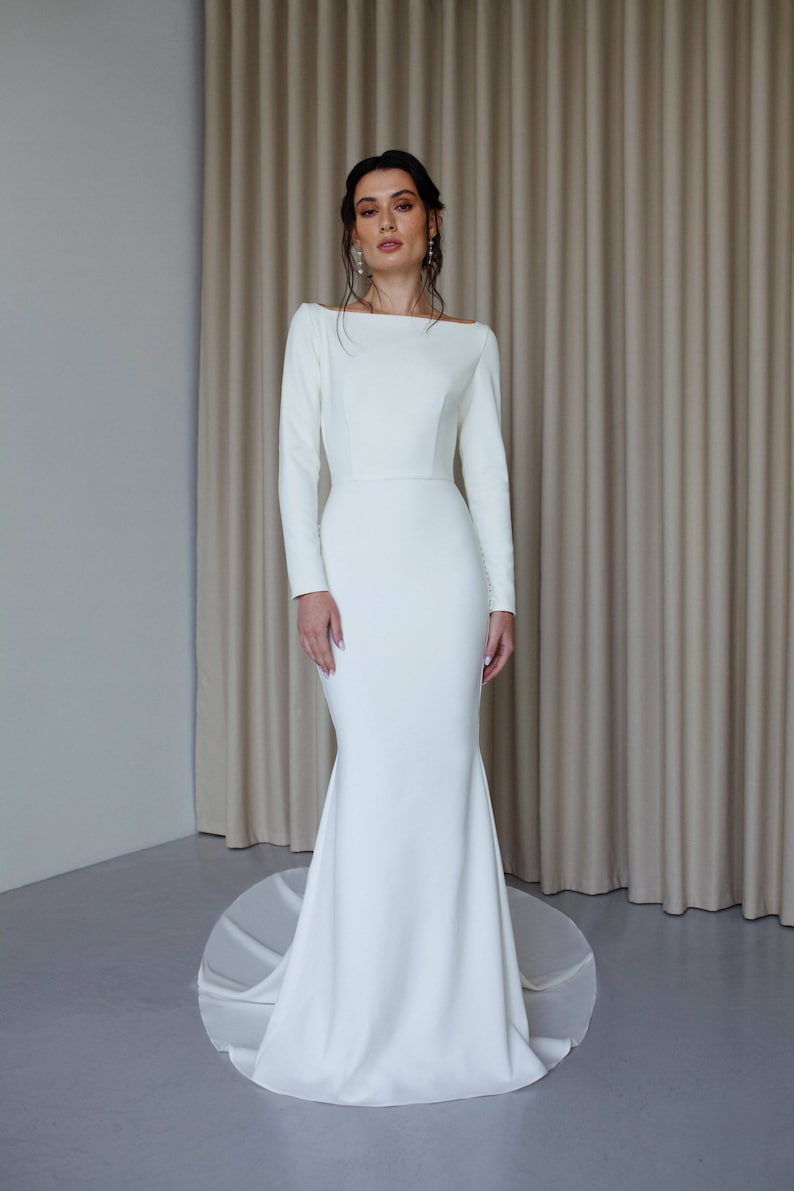 May include: A white, long-sleeved wedding dress with a fitted bodice and a flowing skirt.