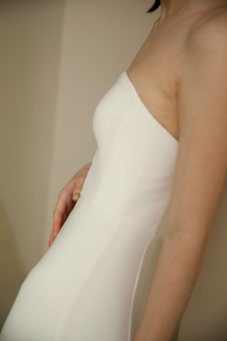Puede incluir: Un vestido blanco sin tirantes con un corpi&ntilde;o ajustado y una falda fluida.