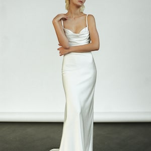Peut inclure: Une robe blanche en satin avec un d&eacute;collet&eacute; en col roul&eacute; et des bretelles spaghetti. La robe a un corsage ajust&eacute; et une jupe fluide.