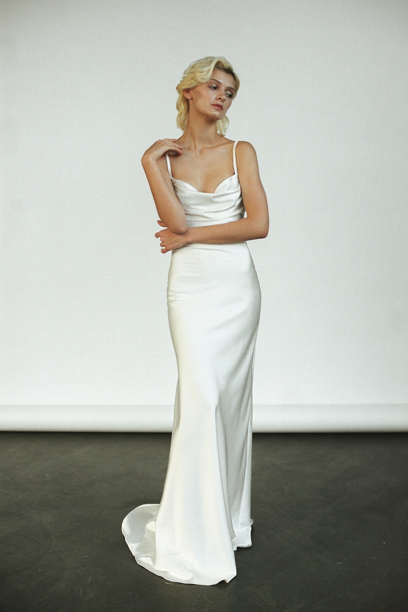 Peut inclure: Une robe blanche en satin avec un d&eacute;collet&eacute; en col roul&eacute; et des bretelles spaghetti. La robe a un corsage ajust&eacute; et une jupe fluide.