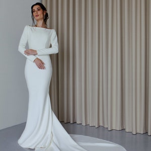 May include: A white long-sleeved wedding dress with a fitted bodice and a flowing train. The dress is made of a smooth, satin-like fabric.