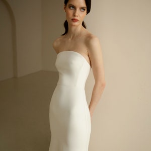 Puede incluir: Una mujer con un vestido de novia blanco sencillo y sin tirantes, con un corpi&ntilde;o ajustado y una falda fluida.