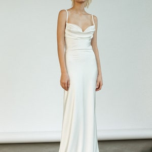 Peut inclure: Une robe de mari&eacute;e blanche en satin &agrave; col en cowl et fines bretelles. La robe a un corsage ajust&eacute; et une jupe fluide.