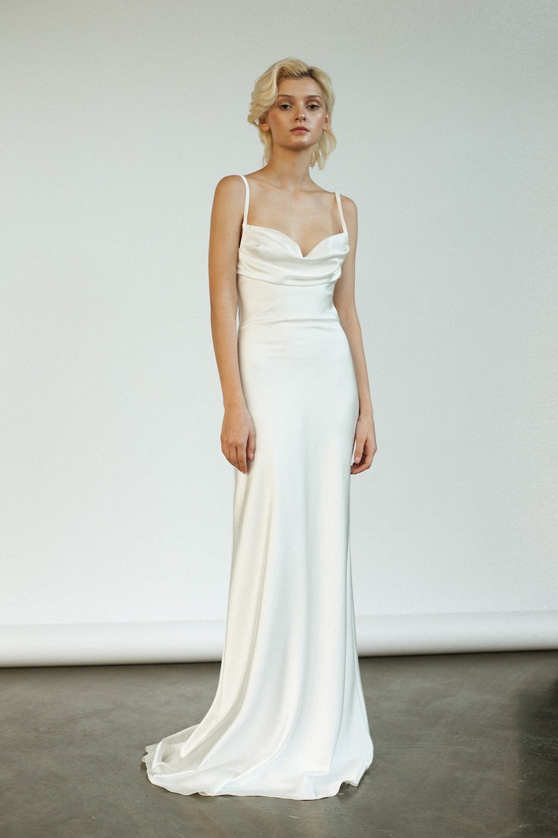 Peut inclure: Une robe de mari&eacute;e blanche en satin &agrave; col en cowl et fines bretelles. La robe a un corsage ajust&eacute; et une jupe fluide.