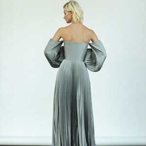 May include: A light gray, off-the-shoulder, pleated maxi dress with a fitted bodice and voluminous sleeves.