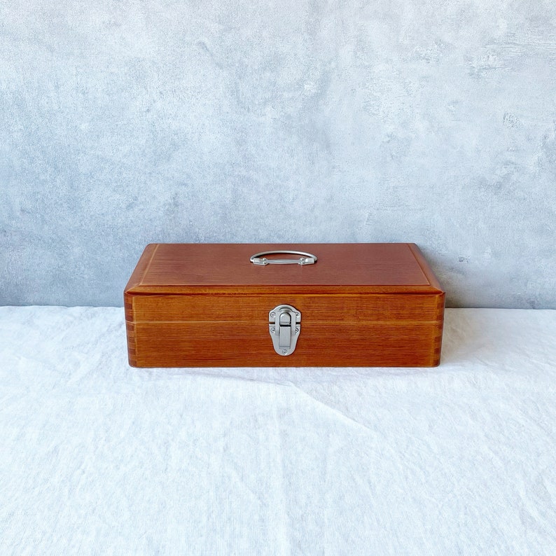 May include: A wooden box with a metal latch and handle. The box is brown and has a natural wood finish.