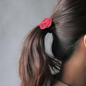 Puede incluir: Una liga para el pelo de tela roja con forma de rosa, atada en una coleta.