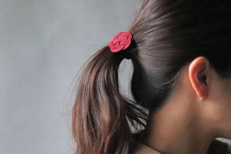 Puede incluir: Una liga para el pelo de tela roja con forma de rosa, atada en una coleta.