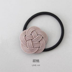 Puede incluir: Una liga para el pelo de tela rosa con un nudo decorativo en forma de flor. La liga para el pelo est&aacute; sobre un fondo blanco. El texto "UME-H4" est&aacute; debajo de la liga para el pelo.