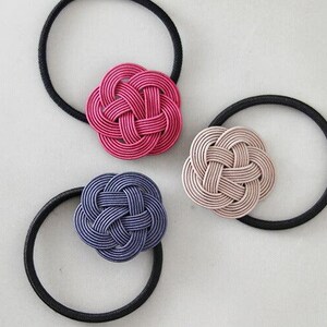 Puede incluir: Tres gomas para el pelo con flores de tela anudadas decorativas. Las flores son de color rosa, rosa claro y azul oscuro.