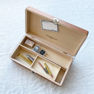 May include: A wooden box with a hinged lid, open to reveal a variety of art supplies. The box contains two pencils, a ruler, a small metal tool, and two ink pads. The box is labeled "Handle with Care, Crafted with Love in Classic."