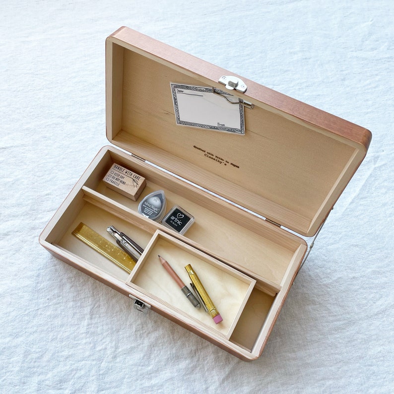 May include: A wooden box with a hinged lid, open to reveal a variety of art supplies. The box contains two pencils, a ruler, a small metal tool, and two ink pads. The box is labeled "Handle with Care, Crafted with Love in Classic."