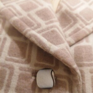Puede incluir: Primer plano de una chaqueta beige con un patr&oacute;n geom&eacute;trico blanco. La chaqueta tiene un solo bot&oacute;n blanco con un contorno negro.