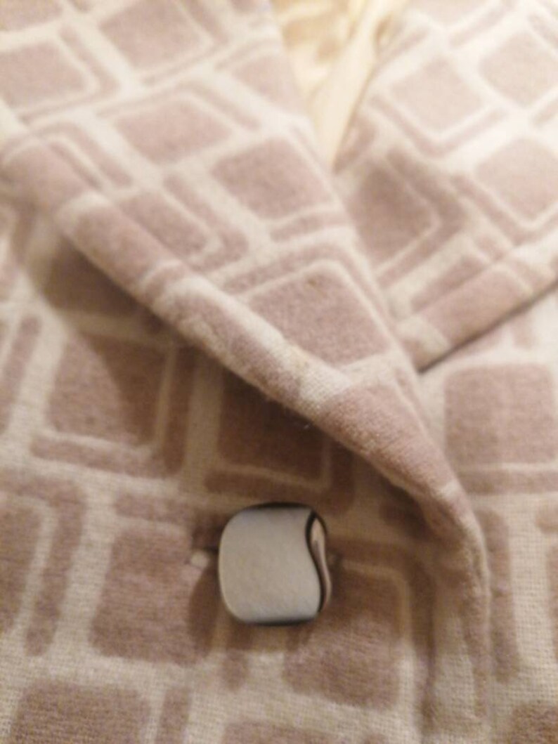 Puede incluir: Primer plano de una chaqueta beige con un patr&oacute;n geom&eacute;trico blanco. La chaqueta tiene un solo bot&oacute;n blanco con un contorno negro.