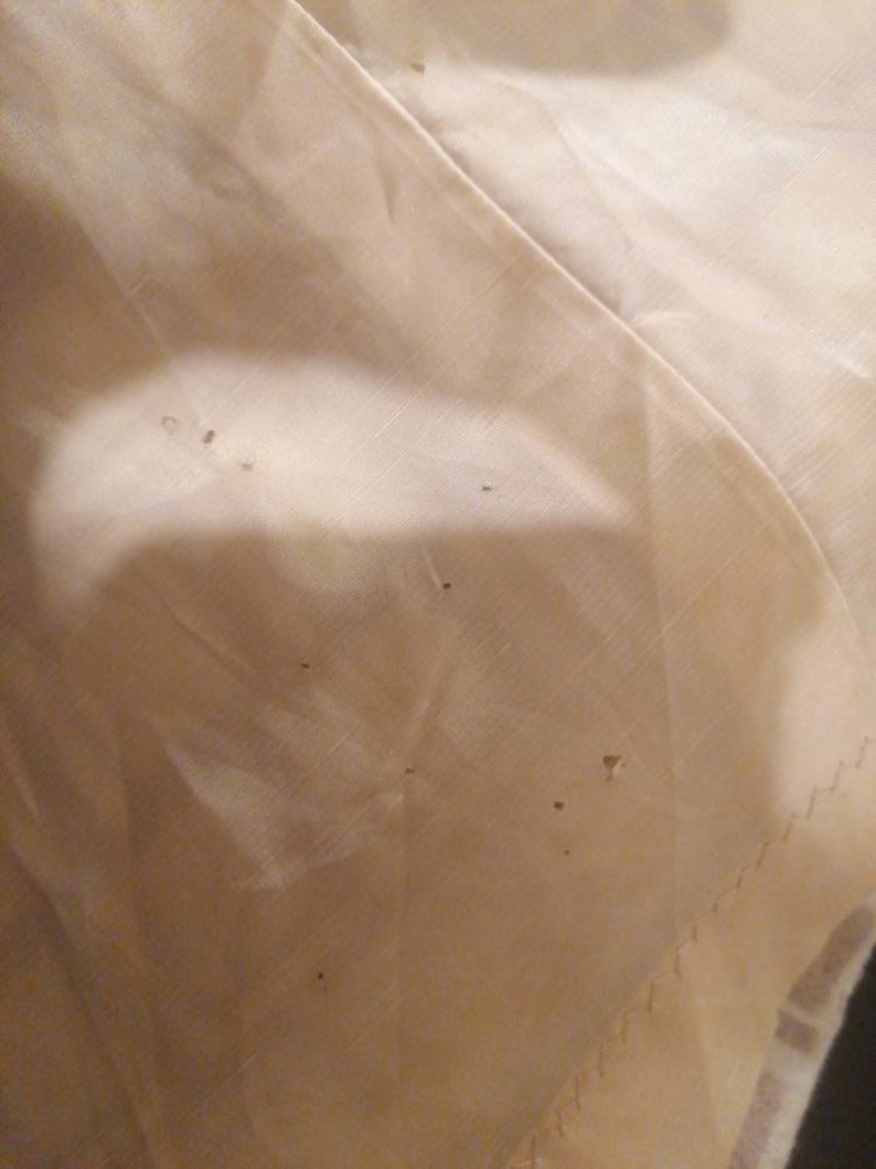 Puede incluir: Primer plano de una tela de color crema con varios agujeros peque&ntilde;os. La tela tiene una textura sutil y una apariencia ligeramente arrugada.