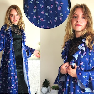 Puede incluir: Una larga bata azul floral con ribetes de volantes y mangas largas. La bata tiene un estampado floral con flores rosas y blancas sobre un fondo azul.