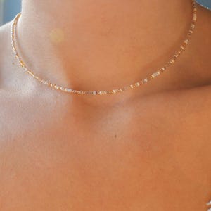 May include: A delicate gold and white beaded necklace. The necklace is made of small, round beads that are strung together to create a simple and elegant design.