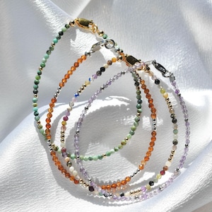 May include: Several delicate beaded bracelets in shades of green, orange, purple, and neutral tones. The bracelets feature small, colorful beads interspersed with silver and gold accents. Each bracelet has a clasp closure.